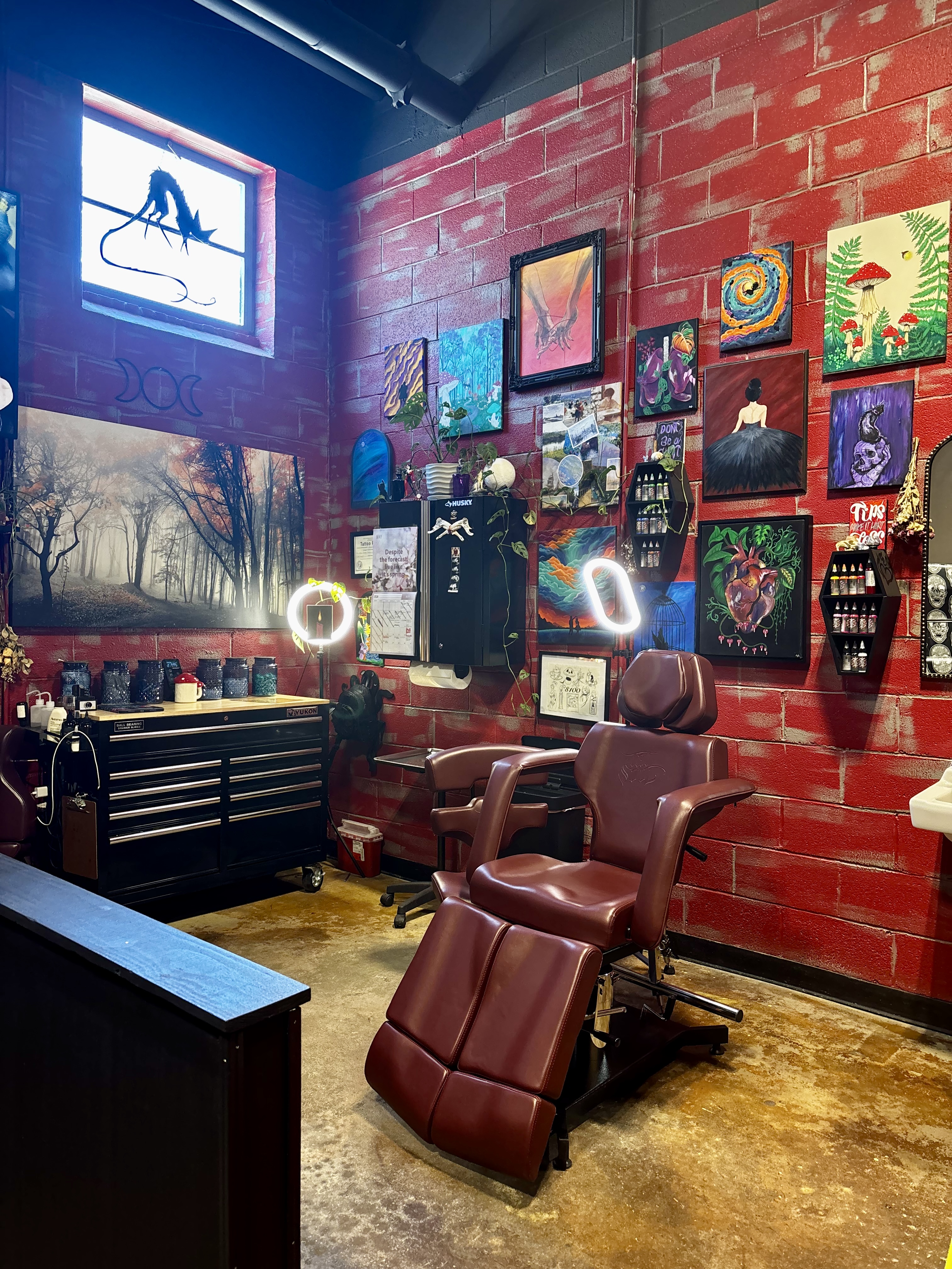 Katt Garner's studio corner at Blue Ridge Tattoo Co. — red brick walls lined with original paintings